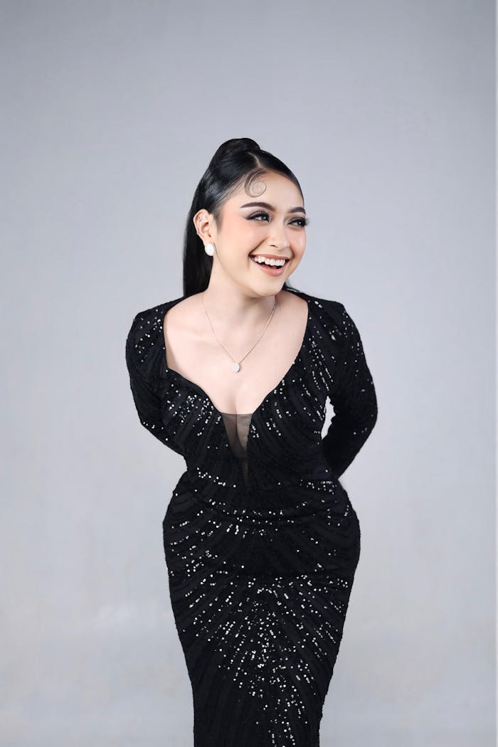 Chic woman in a shimmering black dress, laughing joyfully. Perfect for fashion and glamour themes.